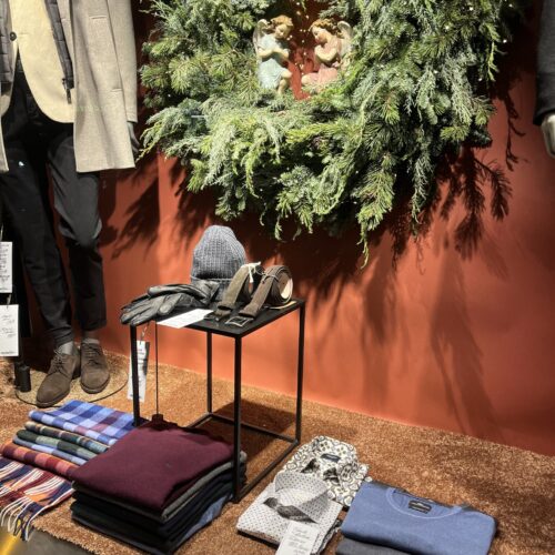 Schaufenster mit Kleidung, Schal, Handschuhen und grünem Kranz auf rotem Hintergrund.