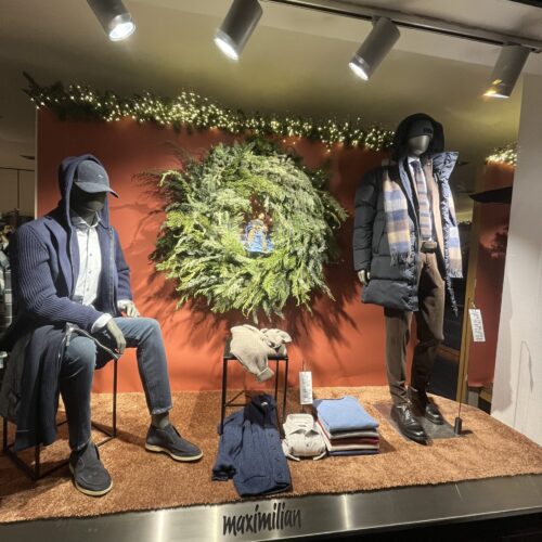 Schaufenster mit Herbstmode auf zwei Mannequins, umgeben von grünem Kranz auf rotem Hintergrund.