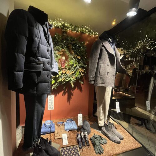 Zwei Schaufensterpuppen in Winterkleidung, dekoriert mit Handschuhen, Hüten und festlichem Grün.