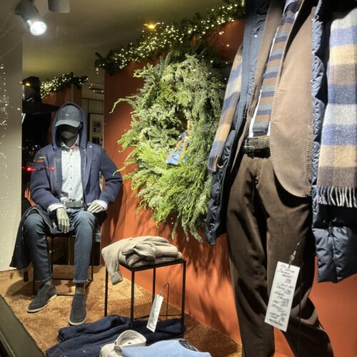 Schaufenster mit zwei Schaufensterpuppen in eleganter Winterkleidung, umgeben von Dekorationen.