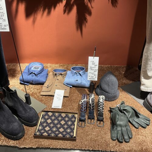 Schaufenster mit blauen und beigen Accessoires, wie Mützen und Handschuhen; rustikale Gestaltung.