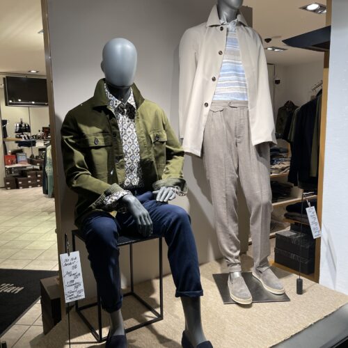 Zwei Schaufensterpuppen mit eleganten Outfits, eine in olivgrüner Jacke, die andere in beiger Jacke.