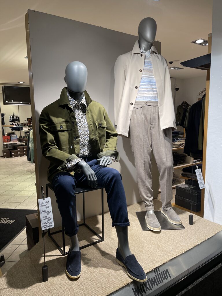 Zwei Schaufensterpuppen mit eleganten Outfits, eine in olivgrüner Jacke, die andere in beiger Jacke.