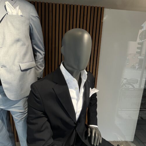 Eine Schaufensterpuppe im schwarzen Anzug und weißem Hemd mit Einstecktuch sitzt elegant