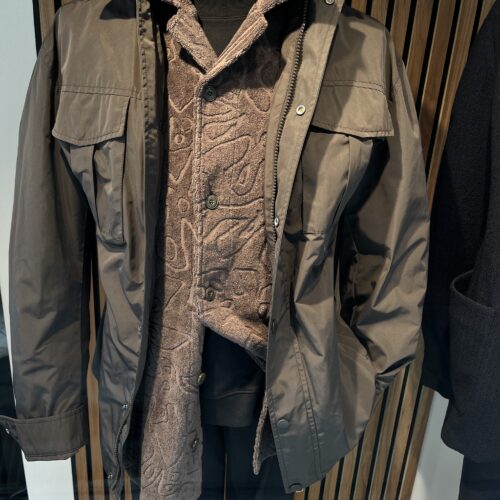 Eine Schaufensterpuppe trägt eine braune Jacke über einem gemusterten Hemd und schwarzer Hose