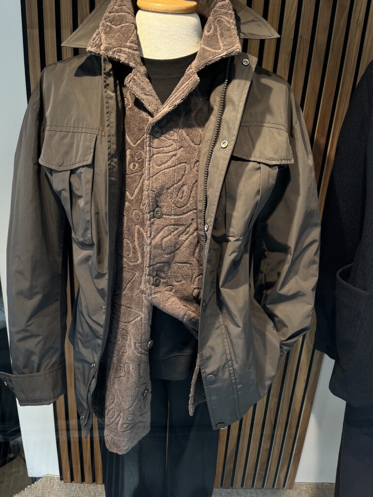 Eine Schaufensterpuppe trägt eine braune Jacke über einem gemusterten Hemd und schwarzer Hose