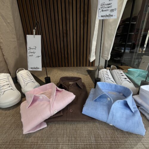 Drei Hemden in Rosa, Braun und Hellblau liegen ordentlich neben weißen Sneakers arrangiert