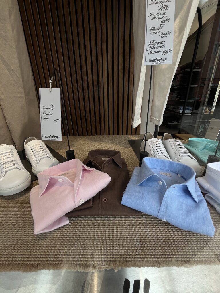 Drei Hemden in Rosa, Braun und Hellblau liegen ordentlich neben weißen Sneakers arrangiert