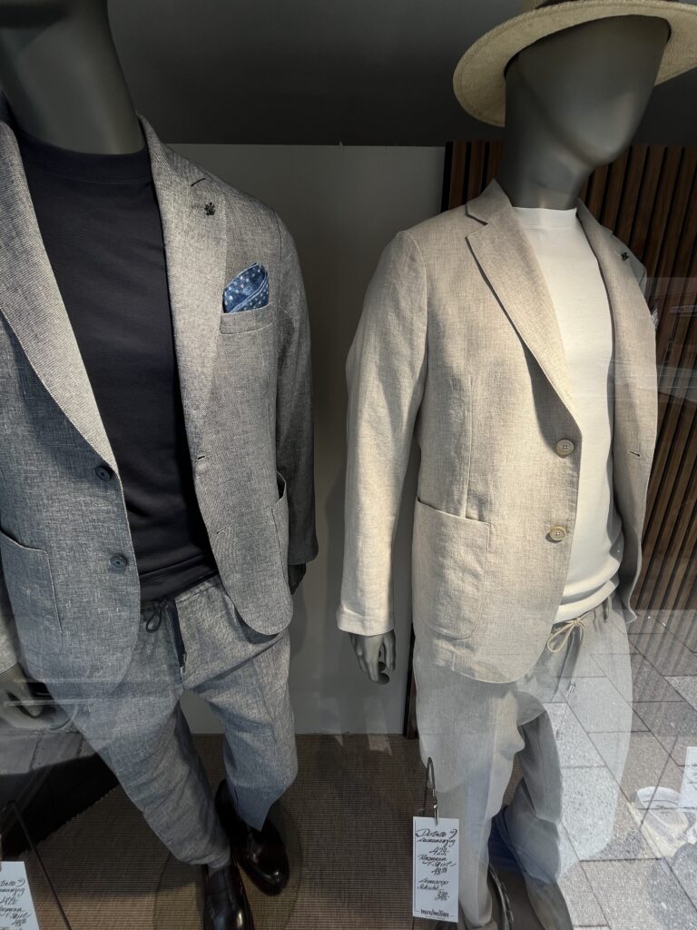 Zwei Schaufensterpuppen tragen helle Anzüge und schauen mit neutralem Gesicht