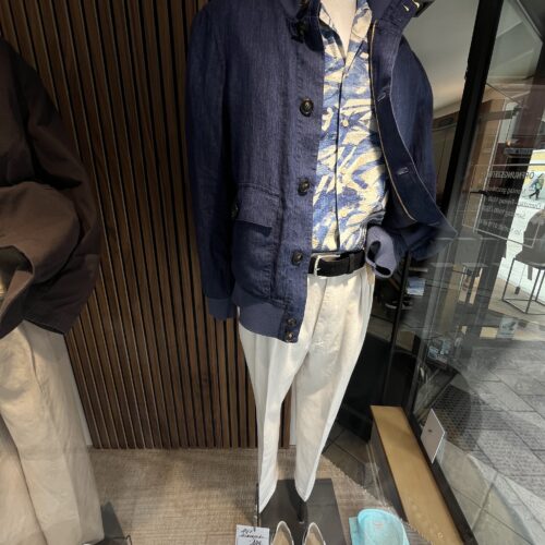 Ein Schaufensterpuppe trägt eine blaue Jacke, ein gemustertes Hemd und helle Hosen