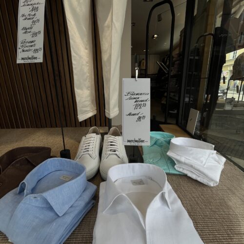 Ein Schaufenster zeigt weiße Hemden, blaue Hemden, Sneakers und beige Hosen