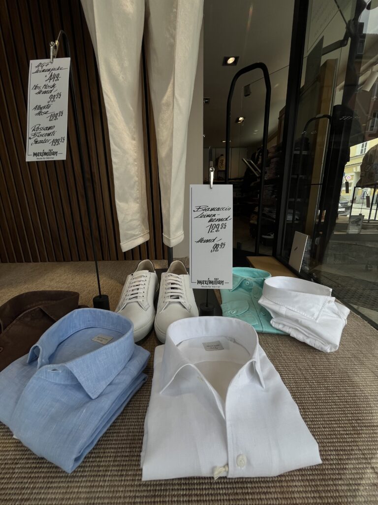 Ein Schaufenster zeigt weiße Hemden, blaue Hemden, Sneakers und beige Hosen